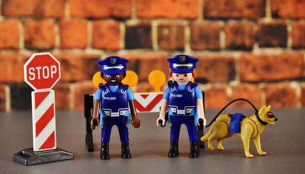 Zwei Playmobil Figuren in Polizeiuniform, davon eine person of colour. rechts daneben steht ein angeleinter Playmobil-Polizeihund.